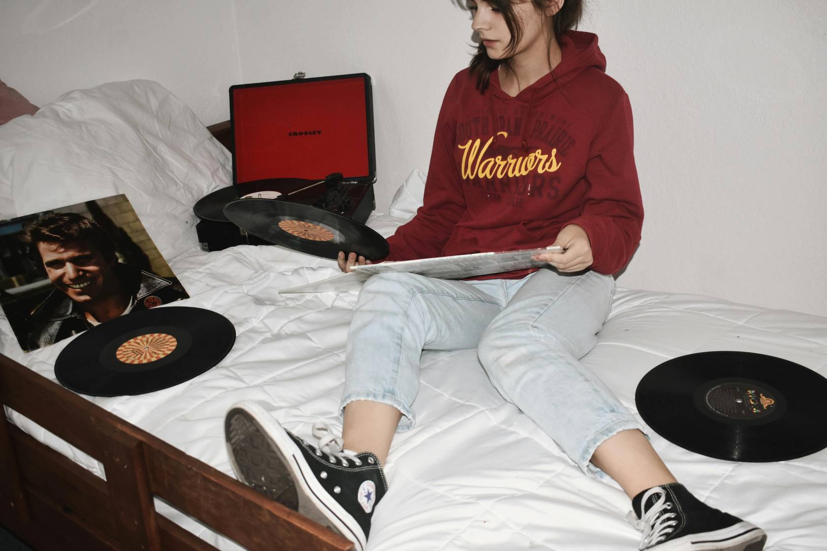 Person sitting comfortably on a couch while wearing pants and outerwear, with wrist resting on elbow. Shoes visible. Text reads "CROSLEY".